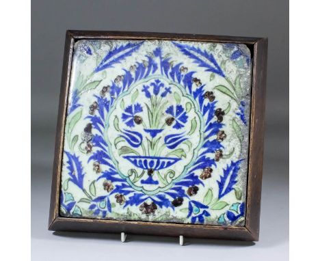 A 17th Century Iznik pottery tile painted in underglaze enamels with a vase of flowers within a shaped cartouche, surrounded 
