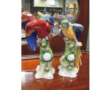 A pair of Sitzendorf models of parakeets, each perched on a rustic leaf and blossoms decorated tree trunk (2) 31cm high  