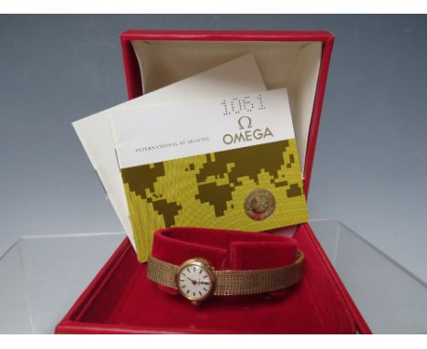 AN OMEGA 9CT GOLD LADIES MANUAL WIND WRISTWATCH, with integral mesh strap, champagne dial with baton markers, in original red