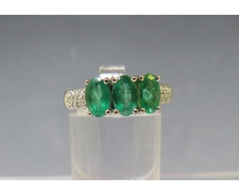 AN 18CT WHITE GOLD 'ILIANA' THREE STONE EMERALD RING, with diamond chip set shoulders, ring size O to O½