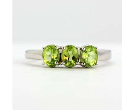 A 9ct white gold ring set with three oval cut peridots, (M).