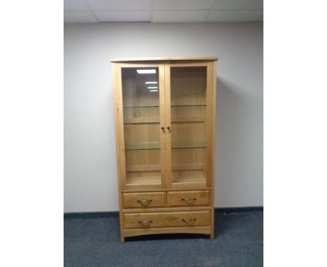 A contemporary light oak display cabinet with three drawers in the base. 