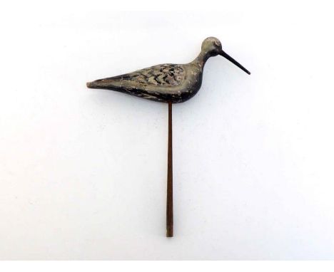 A hand-carved bird decoy on stick stand with long pointed beak and mottled black and grey plumage. Length 38cm. 