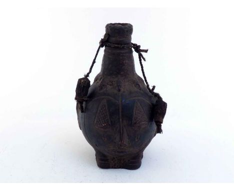 A Nigerian ceramic water flask formed with two masks and two side openings fitted with fabric bound hardwood bungs attached b