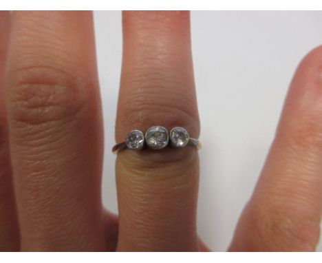 A three stone diamond ring, the three round brilliant cut diamonds in collet mounts with milligrain borders of white metal, s