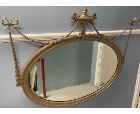 A gilt framed wall mirror of oval form with a central vase and swags