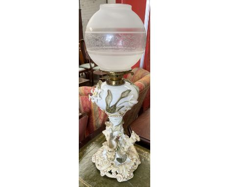 A continental porcelain oil lamp, encrusted with flowerheads and leaves, with a glass globe shade, converted to electricity