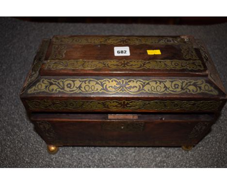 *A Regency rosewood sarcophagus shaped tea caddy with inlaid brass decoration, fitted lion mask handles and brass ball feet, 