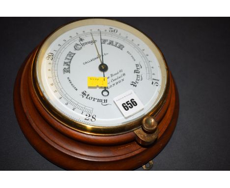 An aneroid barometer in circular brass case, on stained wood turned circular plinth, the dial inscribed "Callaghan & Co., New