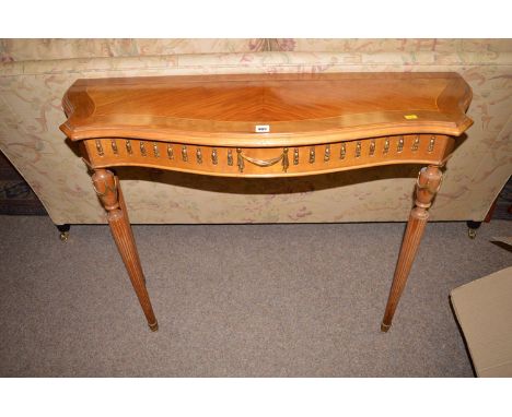 A modern walnut console table of serpentine form with decorative frieze, raised on turned fluted legs.