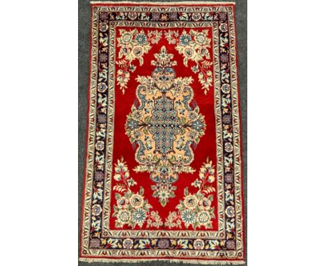 A Central Persian Qum rug / carpet, ornate medallion within a rich red field, stylised floral margin in blue and cream, 170cm