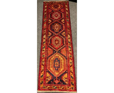 A North West Persian Heriz runner carpet, hand-knotted in rich tones of red, blue, and ochre, with a central row of six hexag