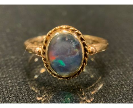 A black opal cabochon ring, vibrant green, blue and orange colour play, rope twist collar, 9ct gold shank, size O, stamped 9c