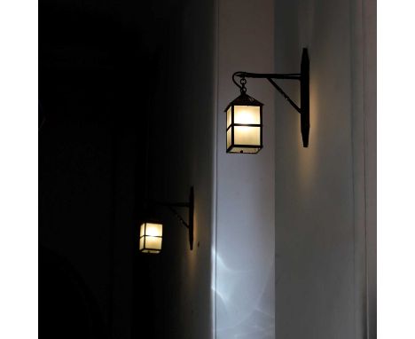 A set of twenty-four black-painted iron wall lanterns, 20th century, each of square form with frosted glass shades, with brac