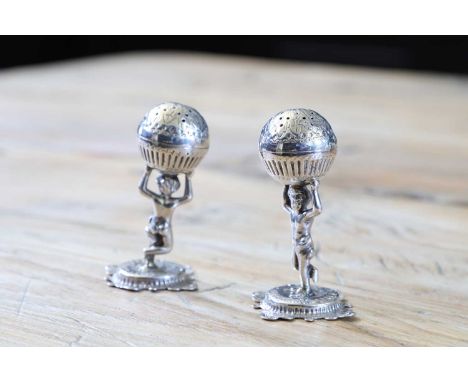 A pair of Victorian silver pepperettes, London 1878,each in the form of a putto supporting a globe, raised on a foliate-chase