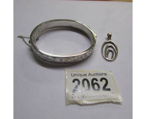 An engraved silver bangle with safety chain and a silver pendant.