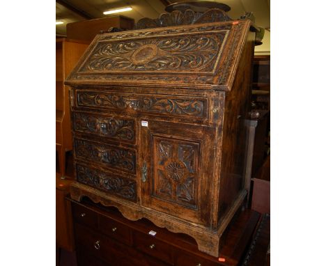 A circa 1900 heavily carved oak slopefront writing bureau, having a carved and raised three-quarter gallery back, the single 