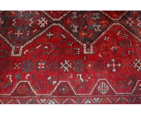 A Persian woollen red ground carpet, the central field decorated with three linked geometric medallions and motifs within tra