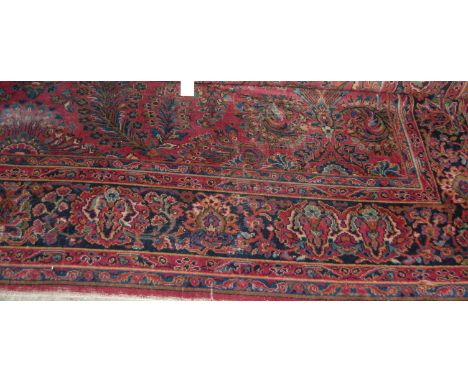 A Persian woollen red ground Tabriz type carpet decorated with stylised flowers and foliage within trailing tramline borders 