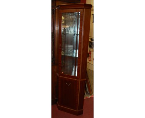 A reproduction mahogany freestanding corner cabinet, having glazed upper door with mirrored interior