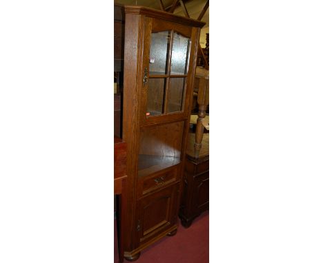 A contemporary moulded oak freestanding corner cupboard, having single glazed upper door