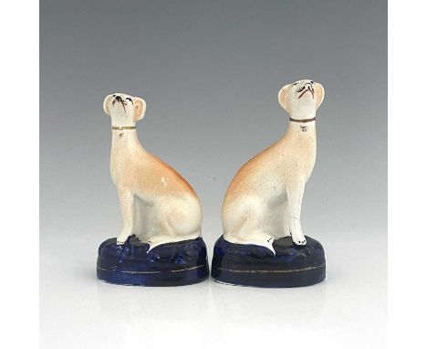 A pair of Staffordshire greyhounds, circa 1860, painted in light brown enamel, seated on cobalt blue oval bases with gilt det