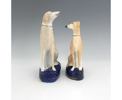Two Staffordshire pearlware greyhounds, circa 1840, painted in light brown enamel, seated on cobalt blue oval bases with gilt