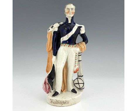 A Staffordshire portrait figure of Wellington, circa 1840, modelled standing in his blue dress uniform with ermine cloak, plu