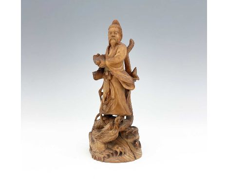 A Chinese carved figure of a scholar, modelled holding a scroll, standing on a writhing dragon, 21cm high