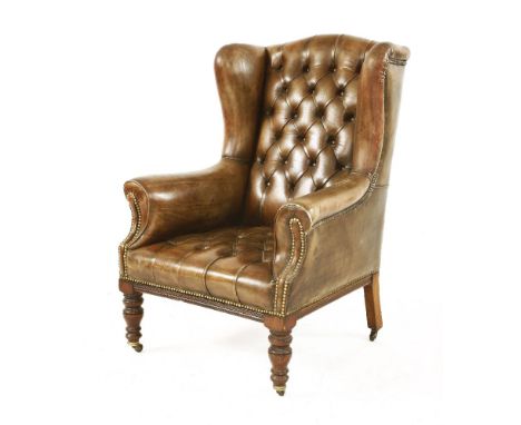 A leather wing-back armchair, with button back and seat, with turned supports