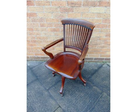 AN EDWARDIAN REVOLVING ELBOW CHAIR  the slatted back and dished seat on quatrefoil support with ceramic casters