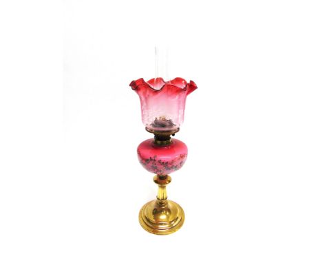 AN EDWARDIAN OIL LAMP  the cranberry glass shade with etched floral decoration, opaque pink glass reservoir, on brass column 