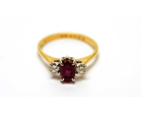 A ruby and diamond cluster ring, the oval facet cut ruby (probably synthetic) flanked by two brilliant cut diamonds, on 18ct 