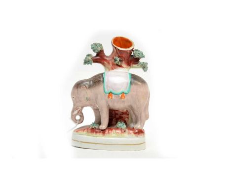 A Staffordshire ceramic spill vase, formed as an elephant standing by a tree, raised on an oval base, 17cms high.