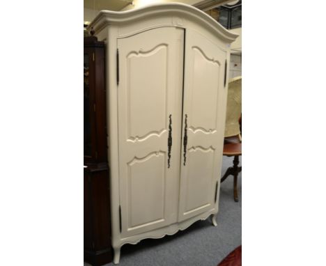 A cream painted armoire of recent date with moulded canopy top above panel doors enclosing hanging space and shelf, 123cm by 