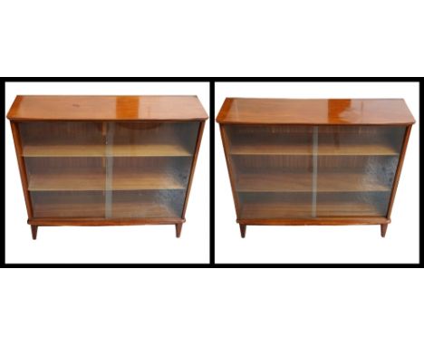 PAIR OF TEAK BOOKCASESwith shaped bow tops above a pair of sliding glass doors enclosing shelves, standing on stout shaped su