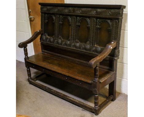 An antique English carved oak bench settle. The back having four panelled niches flanked by geometric decoration, above solid