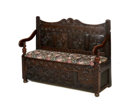 An early 19th century carved oak bench or settle. Having carved panelled back, swept armrests on turned supports, hinged seat