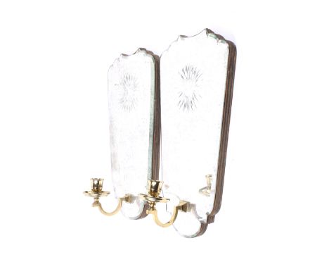 A pair of early 20th century wall mirrors. The bevelled edge mirrors with cut decoration and each featuring a brass candlesti