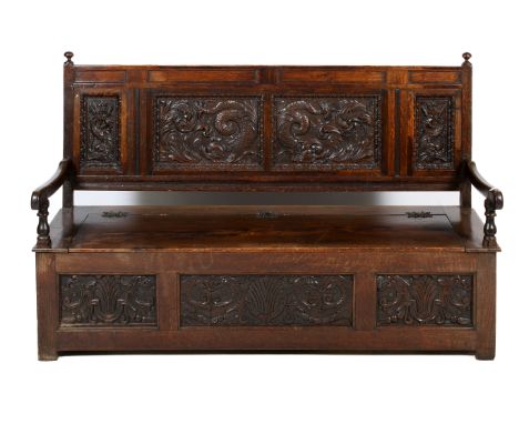 A 19th century carved oak bench settle. Having carved 'dolphin' panelled back, swept armrests on turned supports, hinged seat