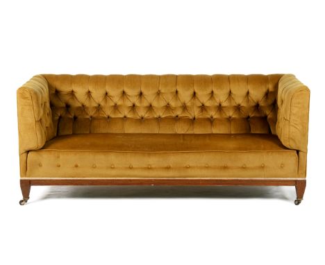 An early 20th century three seater button back settee. Upholstered in a mustard fabric, raised on tapered supports, on brass 