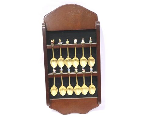 A set of twelve gold plated teaspoons, each finial cast and enamelled with a Beatrix Potter character, with wall rack, maker 