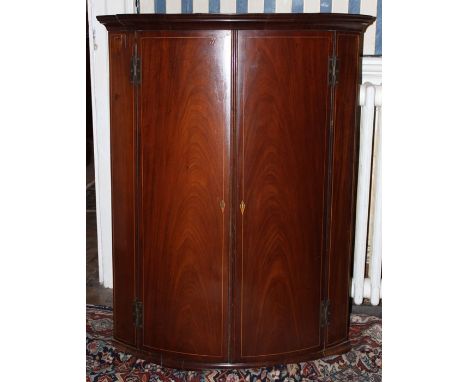 A George III mahogany bow fronted hanging corner cupboard, fitted with two doors enclosing fitted interior, 97cm high