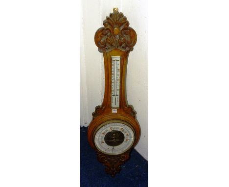 An oak aneroid wall barometer, with carved foliate ends and thermometer above circular weather dial, 89cm long