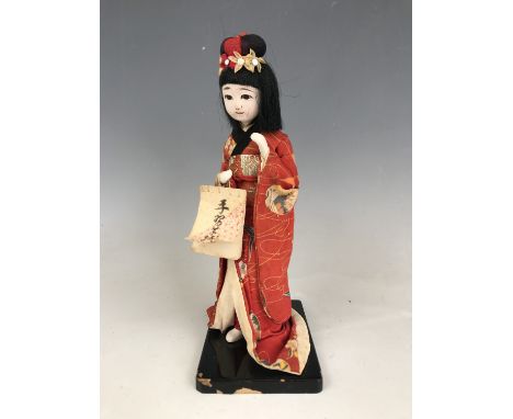 A vintage Japanese figurine of a Geisha, wearing woven and printed cotton robes, over a black lacquered base, 21 cm