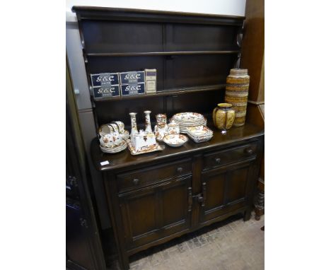 An Ercol Dark Oak Dresser. the dresser having two plate racks, two drawers and panel cupboards beneath on straight feet, appr