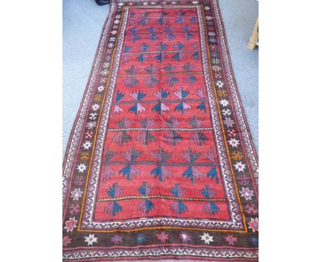 An Afghan Village Rug,  with geometric dsign on a claret background with pink and blue arrow shaped design to central panel, 