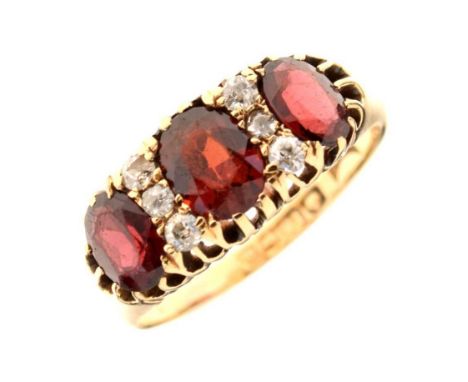 George V 18ct gold three stone garnet ring, the graduated oval cuts with trios of diamonds between, Birmingham 1911, size R, 