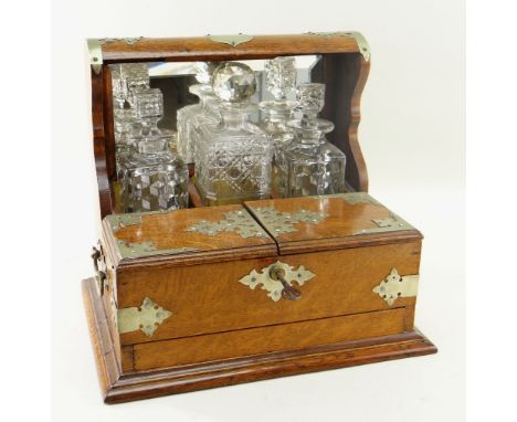 EDWARDIAN OAK TANTALUS, with plated mounts, mirror back and cigar box to the front (refitted), with three associated decanter
