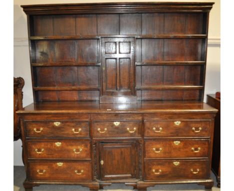 An 18th century oak dresser,
the boarded open plate rack having centre panelled cupboard, the base fitted with drawers and a 